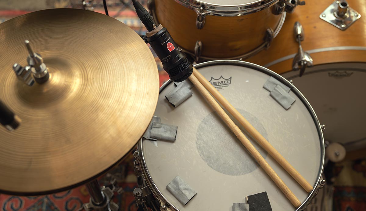 Closeup of a microphone on a snare drum with drum sticks