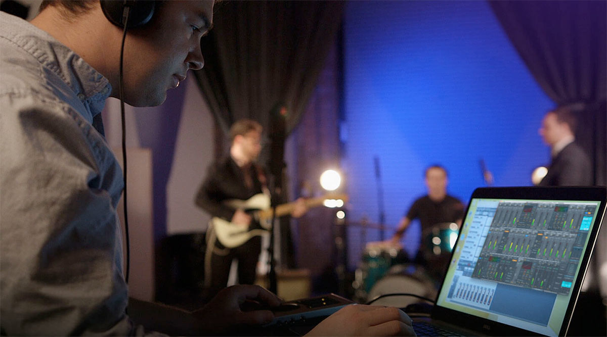 Man using RME TotalMix on a laptop with band performing in background